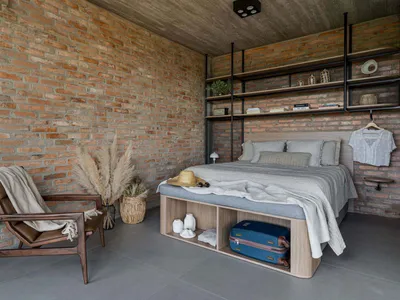 A modern, minimalist bedroom featuring brick and concrete walls, a wooden bed frame, and a leather chair.