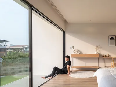 Modern minimalist bedroom with glass wall, wooden floor, and white furniture.