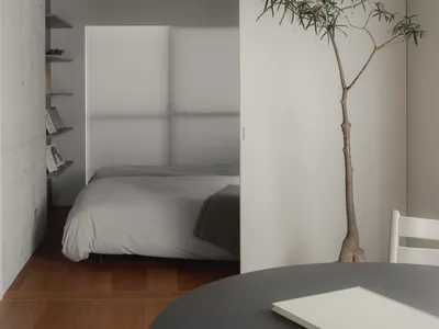 A minimalist bedroom featuring a bed with light-colored sheets on a wood floor.