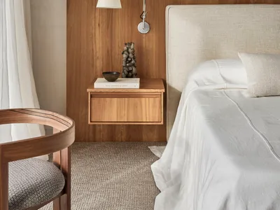 Minimalist bedroom with a fabric nightstand, a bed with an upholstered headboard, and a wall-mounted reading lamp.