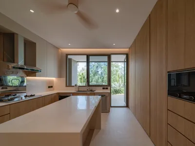 Modern kitchen with minimalist design, featuring wood cabinetry and a white countertop.