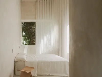 Minimalist bedroom with white curtains, window, and wooden stool