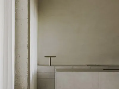 A modern, minimalist kitchen with concrete walls, countertops, and a wooden stool.