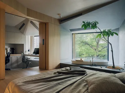 A minimalist bedroom with wood floors, a wooden bed frame, and a large window overlooking greenery.