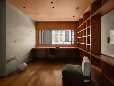 A minimalist study room with wooden furniture, a glass window, and a green cushioned seat.