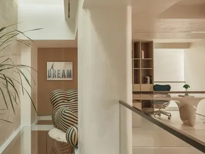 A modern minimalist home office featuring a striped chair, glass desk, and open shelving.