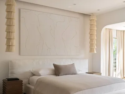 Minimalist bedroom with a large white bed, neutral fabrics, and a geometric patterned rug.
