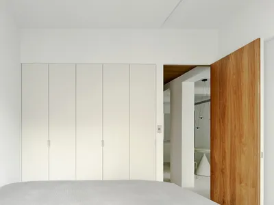 A minimalist bedroom with white walls, a wooden door, and a neatly made bed.