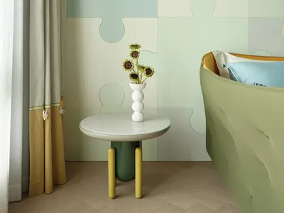 A bedroom featuring a wall covered with fabric panels, a green round table with a vase of sunflowers, and a blue and yellow b
