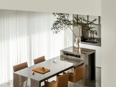 A sleek, modern kitchen dining space featuring marble countertops, brown leather chairs, and a large window allowing natural