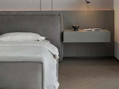 A minimalist bedroom with a neutral color palette, featuring a grey upholstered bed and a floating nightstand with a hanging