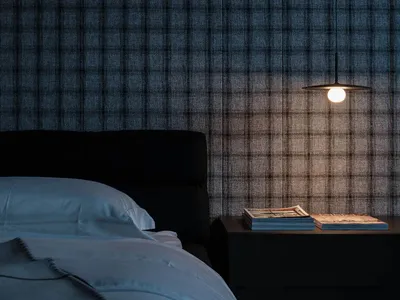 A minimalist bedroom featuring a checkered fabric wall, a black bed with a white blanket, and a hanging pendant light on a be