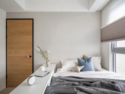 A minimalist bedroom with neutral-toned walls, bedding, and window treatments, featuring a modern wooden door and a sleek whi