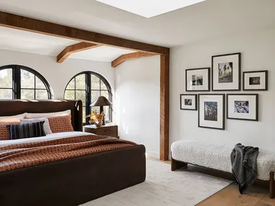 Modern bedroom showcasing a brown leather bed, wooden beams, and framed photographs on the wall.