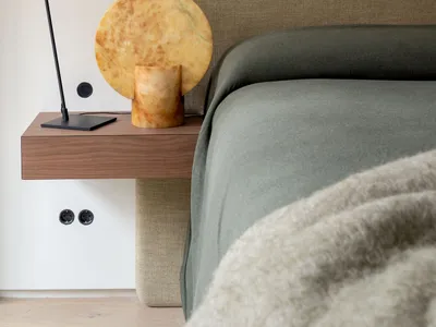 A modern minimalist bedroom featuring a upholstered bed with a large headboard, a floating nightstand with a black lamp and m