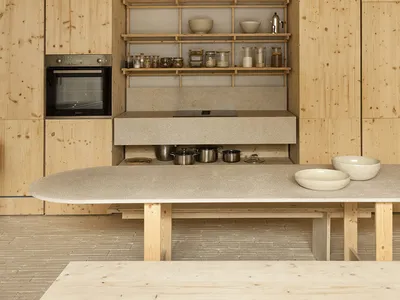 A modern, minimalist kitchen with wooden cabinetry, a concrete countertop, and open shelving.