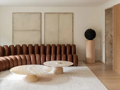 Modern, industrial-style living room with a unique, cushioned leather sofa, round marble tables, and minimalist artwork on th