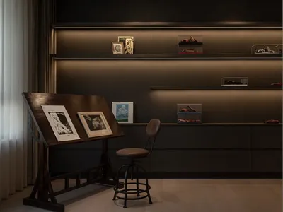 Modern home office with a wooden drafting table, framed artwork, and display shelves with model cars.