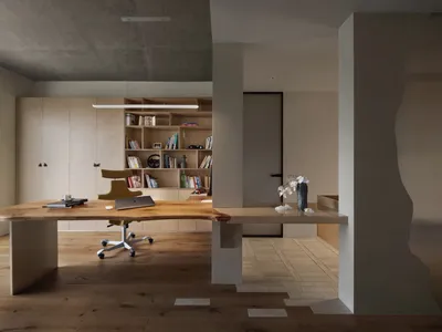 A minimalist home office featuring a wooden desk, steel accents, and floor-to-ceiling bookshelves.