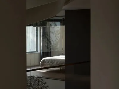 一間極簡現代臥室，擺放床鋪、床邊桌，以及帶有植物的大型窗戶。