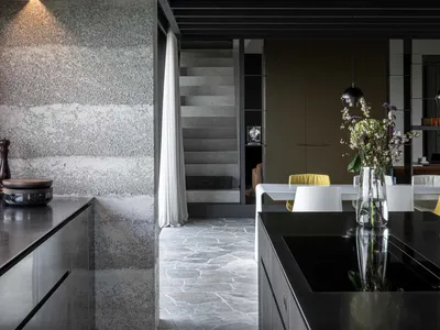Modern kitchen with dark tones, featuring dark cabinets, a black countertop, and a textured gray wall.