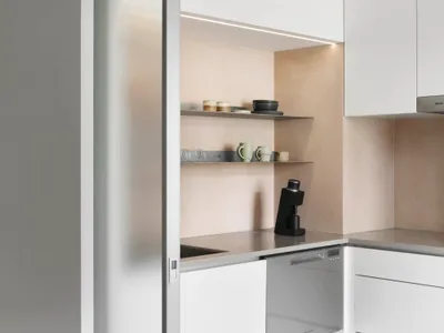 A modern, minimalist kitchen with white cabinets, open shelves, and sleek, clean lines.
