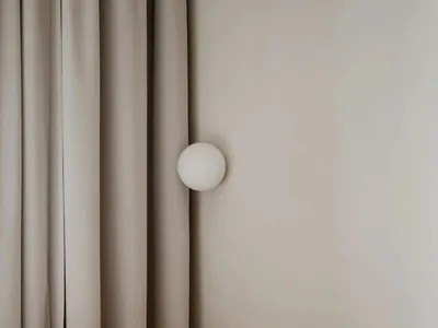 A minimalist bedroom featuring a wood-framed bed against a neutral-colored wall with a simple, spherical light fixture.