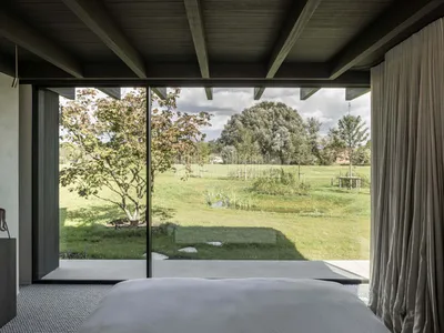 A minimalist bedroom with wood elements and a view of greenery through a large window.