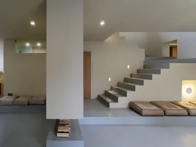 A minimalist living room with concrete walls and stairs, featuring soft seating and a modern design.