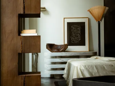 A modern minimalist bedroom featuring a white marble table, a wooden bookshelf, and a dark wood bathtub.