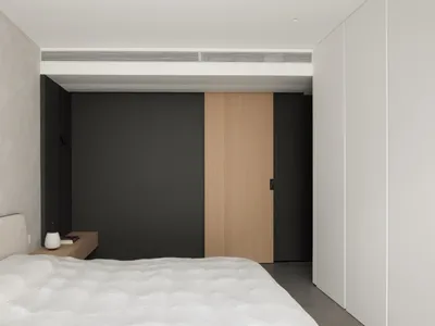 一間現代簡約臥室，配有白色床鋪與簇絨床頭板、小型木質床頭櫃，以及一扇滑門