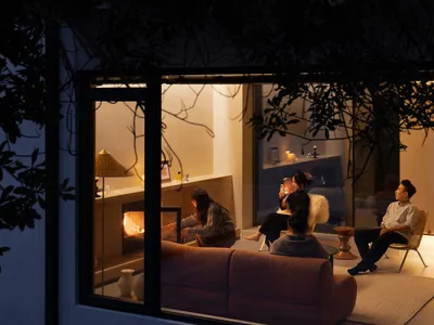 People sitting in a cozy living room at night, illuminated by warm lighting, with a fabric couch and a fireplace.