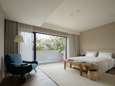 A modern minimalist bedroom with white walls, a neutral color palette, and a large window with curtains.