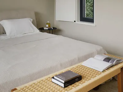 A minimalist bedroom with neutral-toned textiles and a window showing greenery outside.