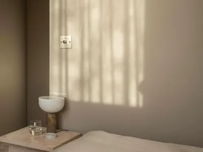 A minimalist bedroom featuring neutral-toned bedding on a bed with a simple, elegant side table.