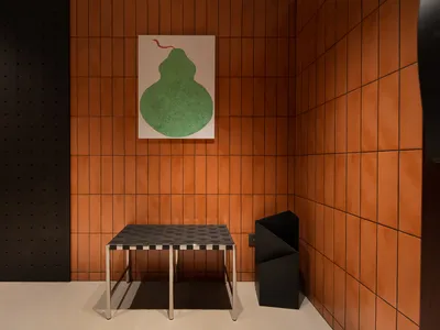 A modern restaurant interior featuring an orange tile wall and a concrete floor with a minimalist metal table and black trash