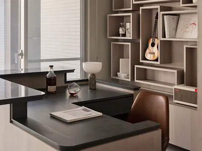 Modern, minimalist home office featuring a sleek desk with a black top and a leather chair. Cube shelves holding books, plant