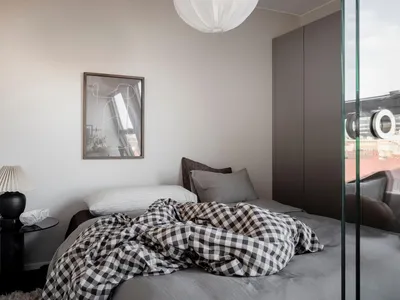 A minimalist bedroom featuring a bed with a checkered blanket, pillows, and a lamp on a bedside table.