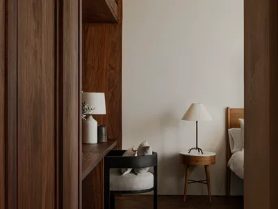 Modern minimalist bedroom with wood furniture, white bedding, and a cozy reading nook.