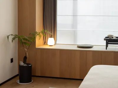 A minimalist bedroom with wooden walls and a cozy reading nook by the window.