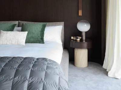 Minimalist bedroom with a bed, green pillows, and a modern lamp on a wooden nightstand.