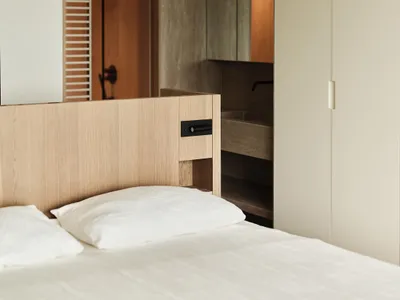Modern minimalist bedroom with wooden headboard and white bedding.