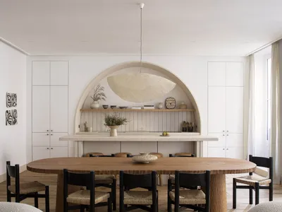A modern, open-plan living and dining room with minimalist decor, wooden furnishings, and a marble counter.