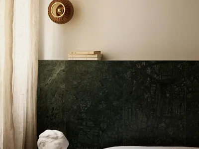 A minimalist bedroom featuring marble walls, a linen curtain, and a wooden bed frame.