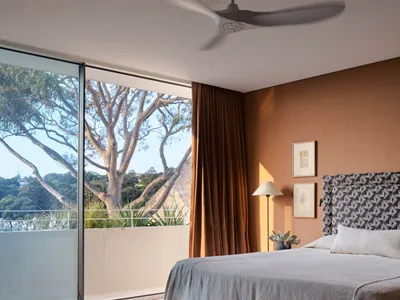 A modern minimalist bedroom featuring linen bedding, wooden headboard, and glass window with a view of outdoor greenery.