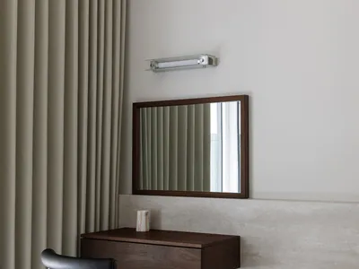 A minimalist bedroom featuring a floating desk with a dark wooden finish, a black chair, and beige curtains.
