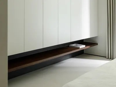 A minimalist bedroom with floating wooden shelves and white walls.