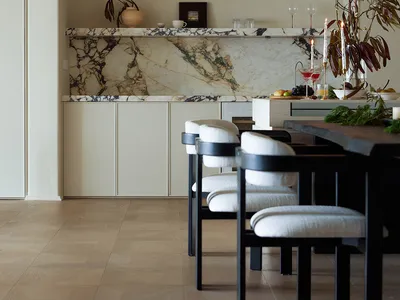 A minimalist dining room featuring a marble counter, white chairs, and a modern light fixture.
