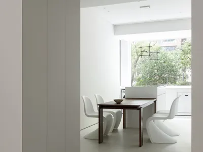 A minimalist kitchen with white cabinets and wood accents, featuring a modern dining table and chairs.