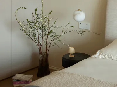 A modern bedroom featuring a bed with a beige cover and a black circular side table with a small white cup on it.
